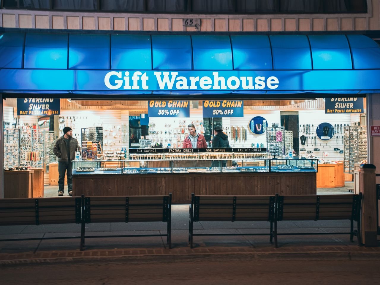journey Night view of Gift Warehouse store with vibrant blue signage and two people inside.