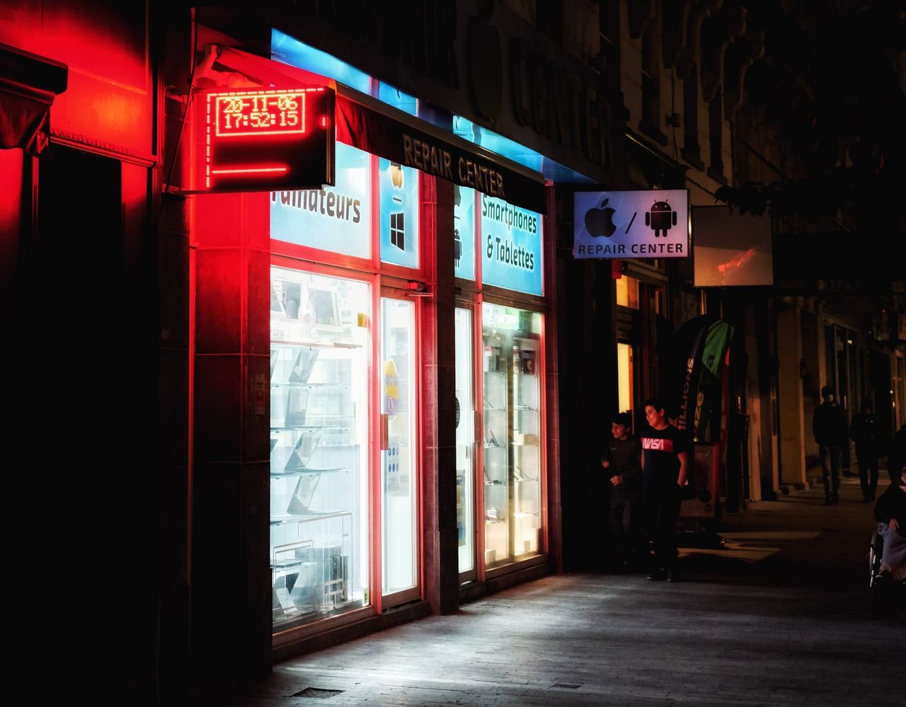 services-01 Vibrant night scene of an illuminated smartphone repair store with red signage.